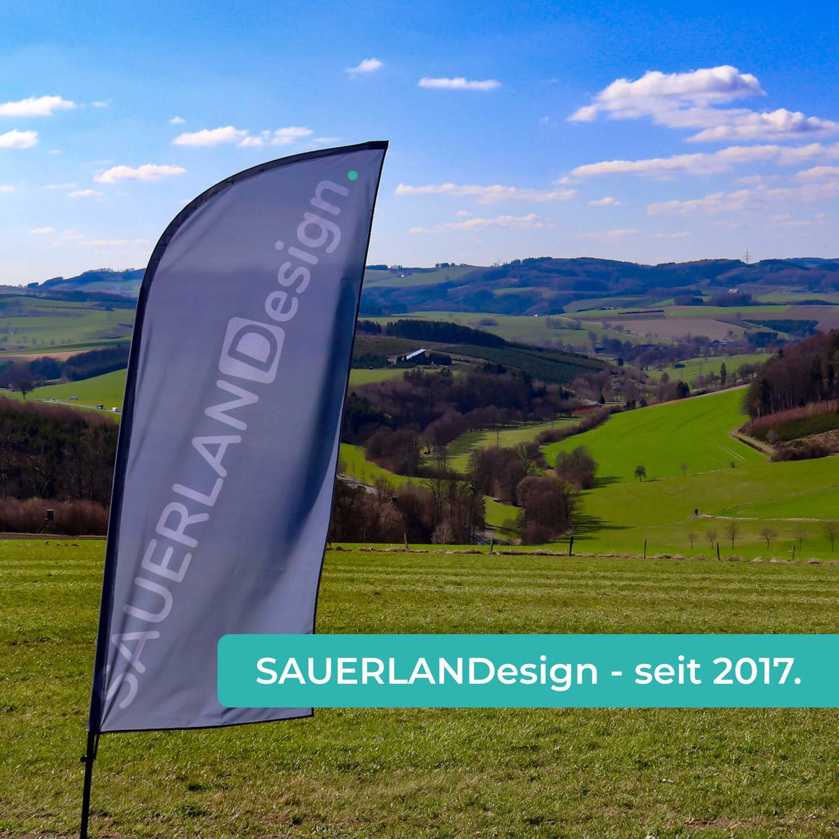 Eine Fahne von SAUERLANDesign ist in der sauerländer Natur. Der Text: SAUERLANDesign - seit 2017 ist lesbar